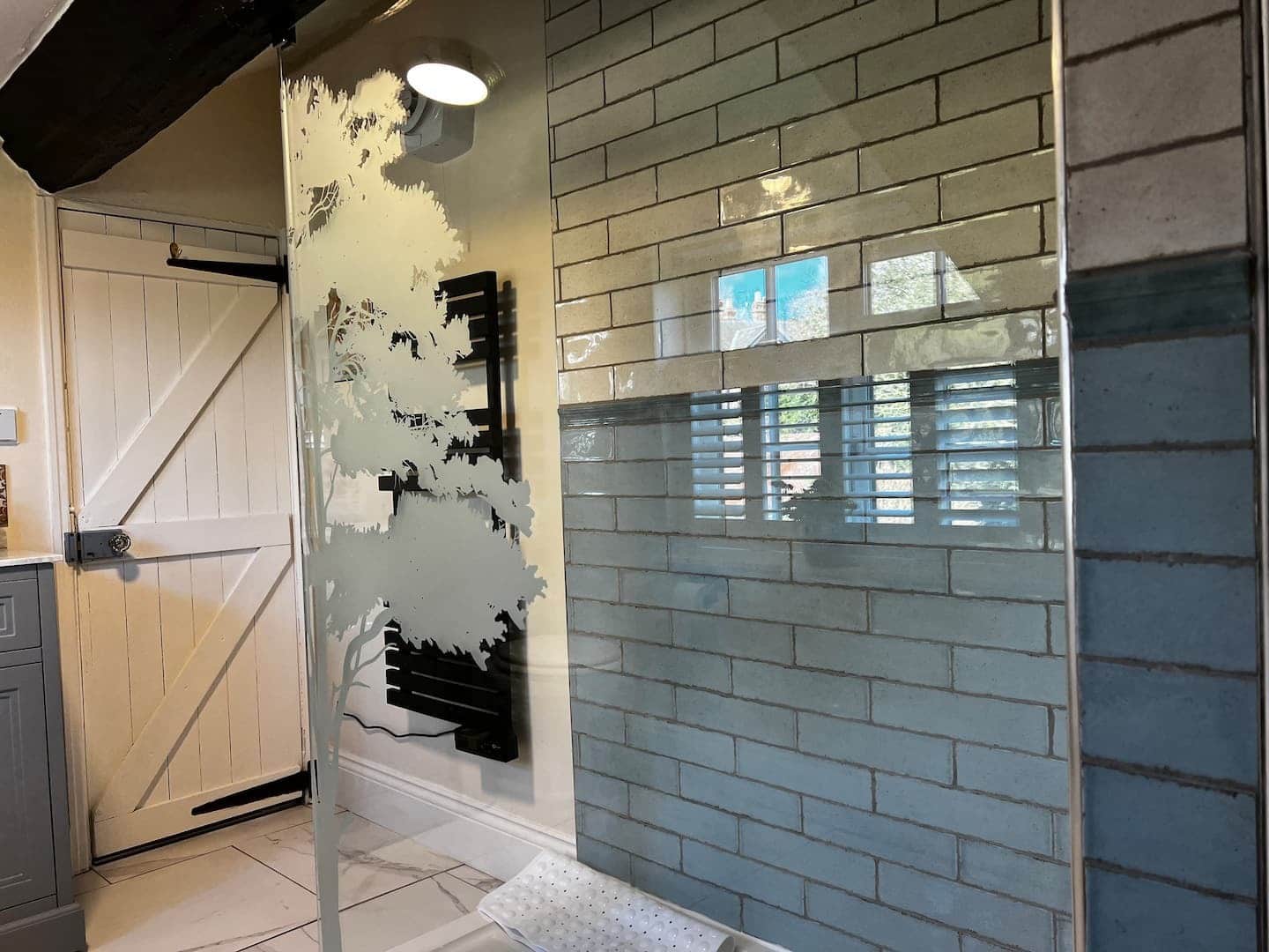 Walk-in shower with an etched-tree glass panel, exposed beams